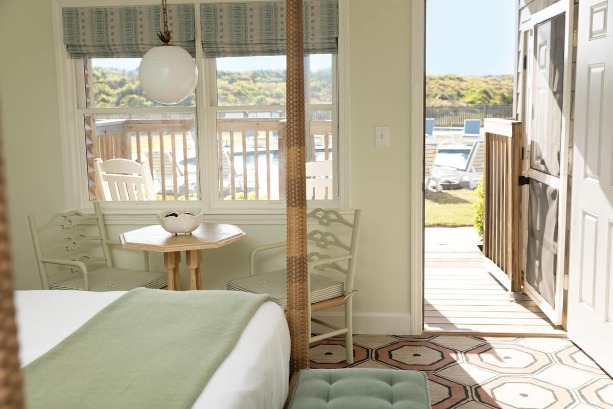 Une chambre avec une grande fenêtre, un lit, une chaise, une petite table et une vue sur la terrasse extérieure.