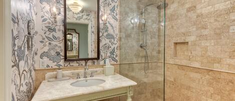 Un baño con lavamanos de mármol, cabina de ducha de vidrio y papel tapiz estampado.