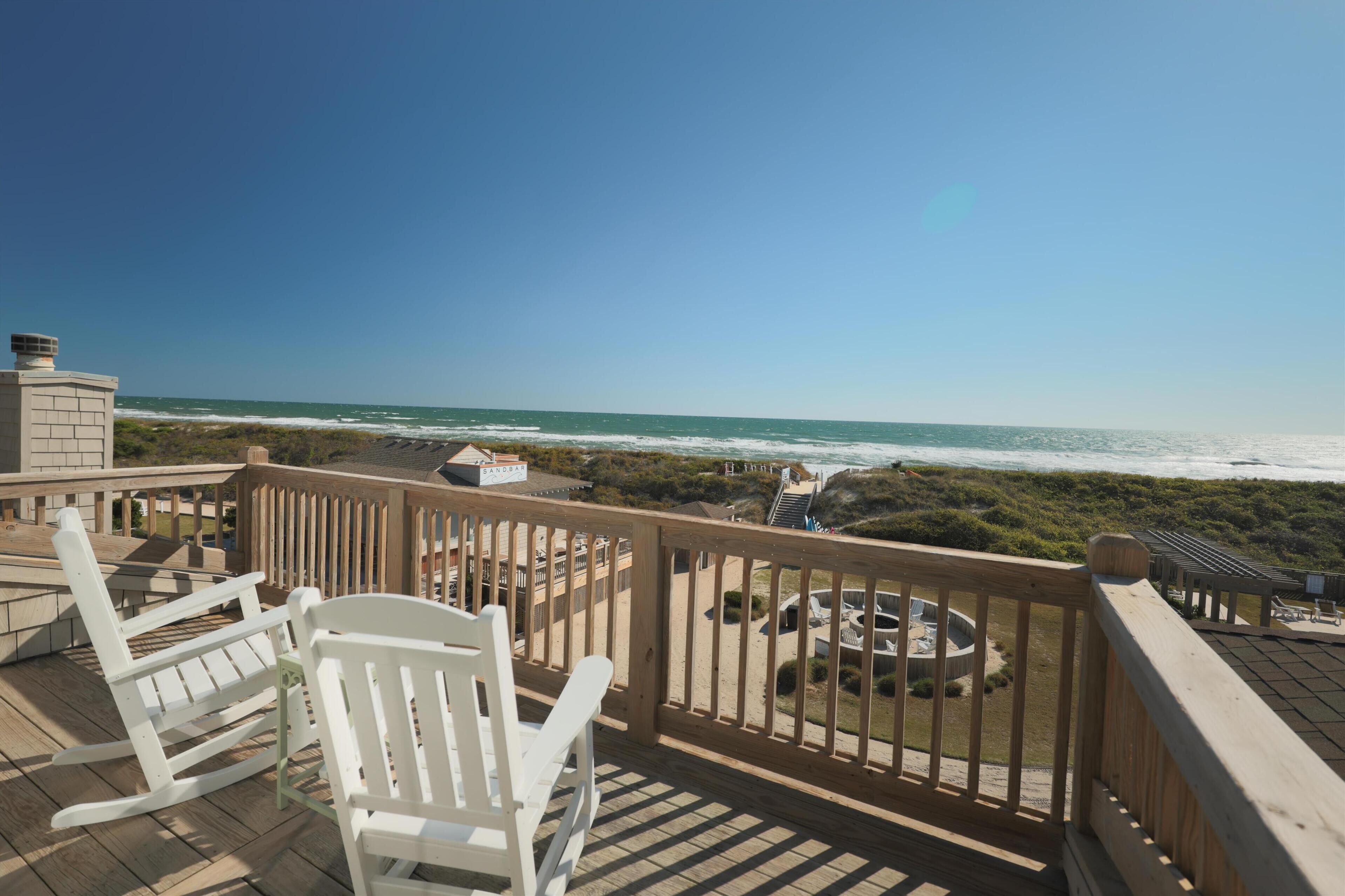 A wooden deck with white rocking chairs overlooking a beach.