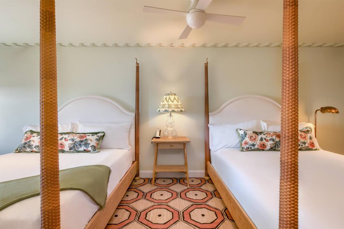 Une chambre avec deux lits, une table de chevet avec une lampe et un ventilateur de plafond.