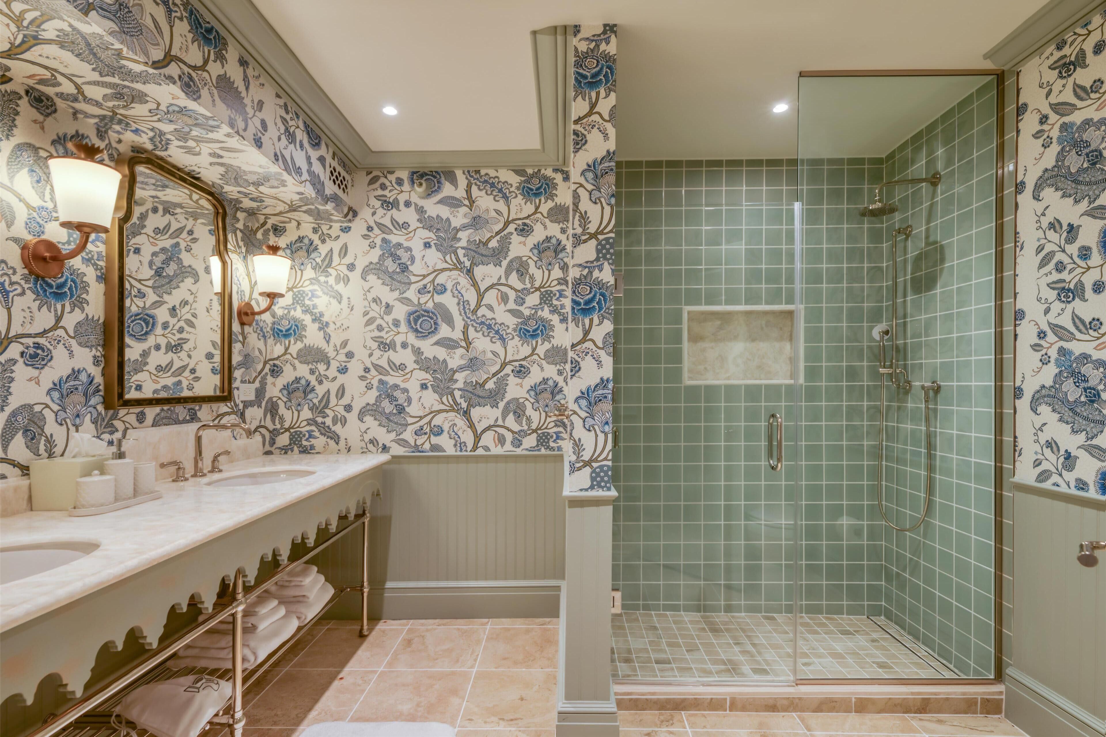 Une salle de bain dotée d’un long meuble-lavabo, de deux vasques, d’un miroir et d’un espace douche séparé par une porte en verre.