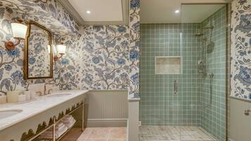Une salle de bain dotée d’un long meuble-lavabo, de deux vasques, d’un miroir et d’un espace douche séparé par une porte en verre.
