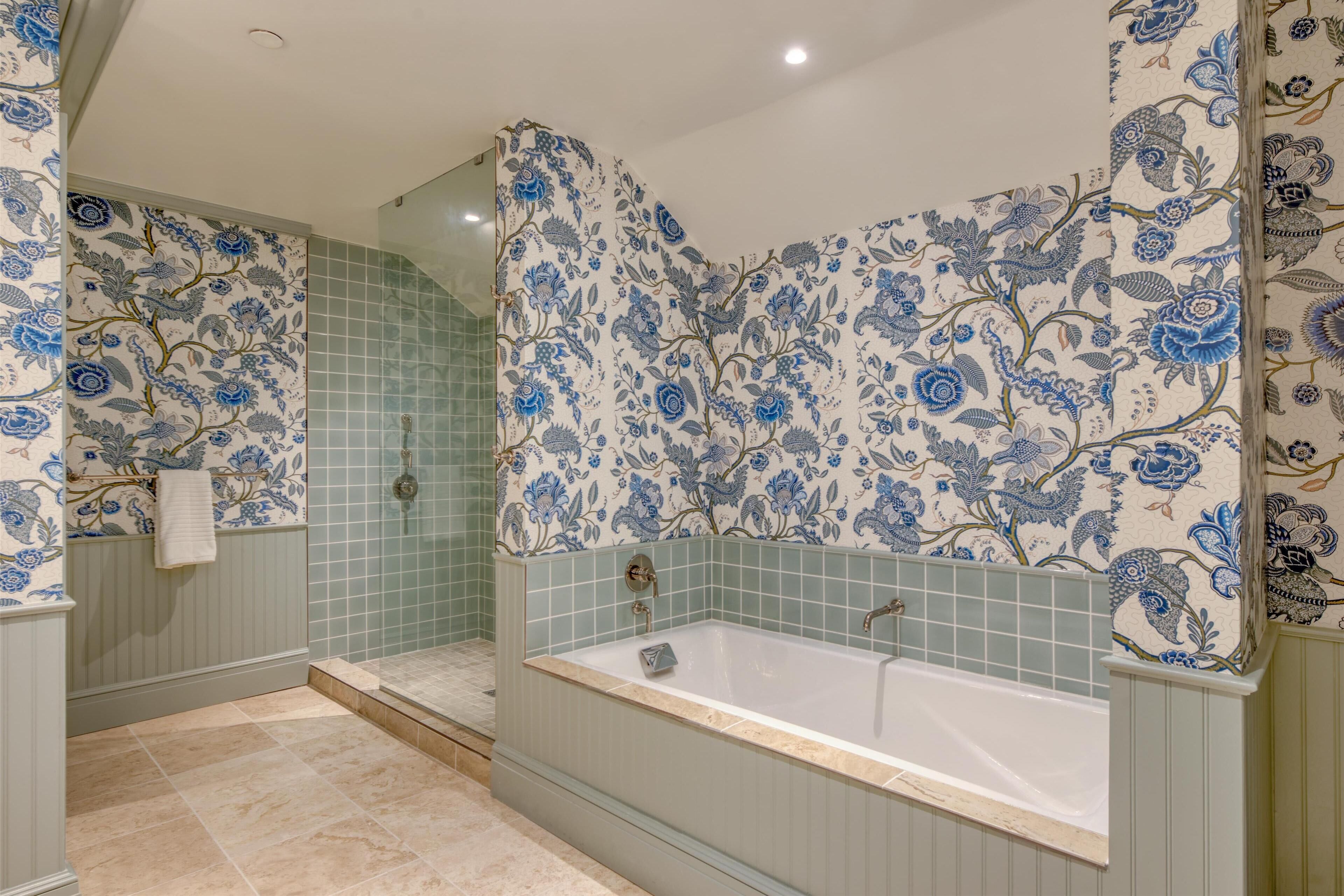 A bathroom with a bathtub, a shower, and floral-patterned walls.