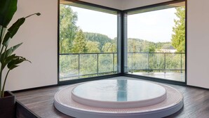 A circular hot tub in a corner with large windows offering a view of a forested hillside.
