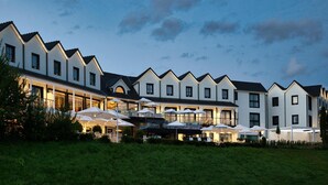 A hotel with multiple white buildings, outdoor seating with umbrellas, and a well-maintained lawn.
