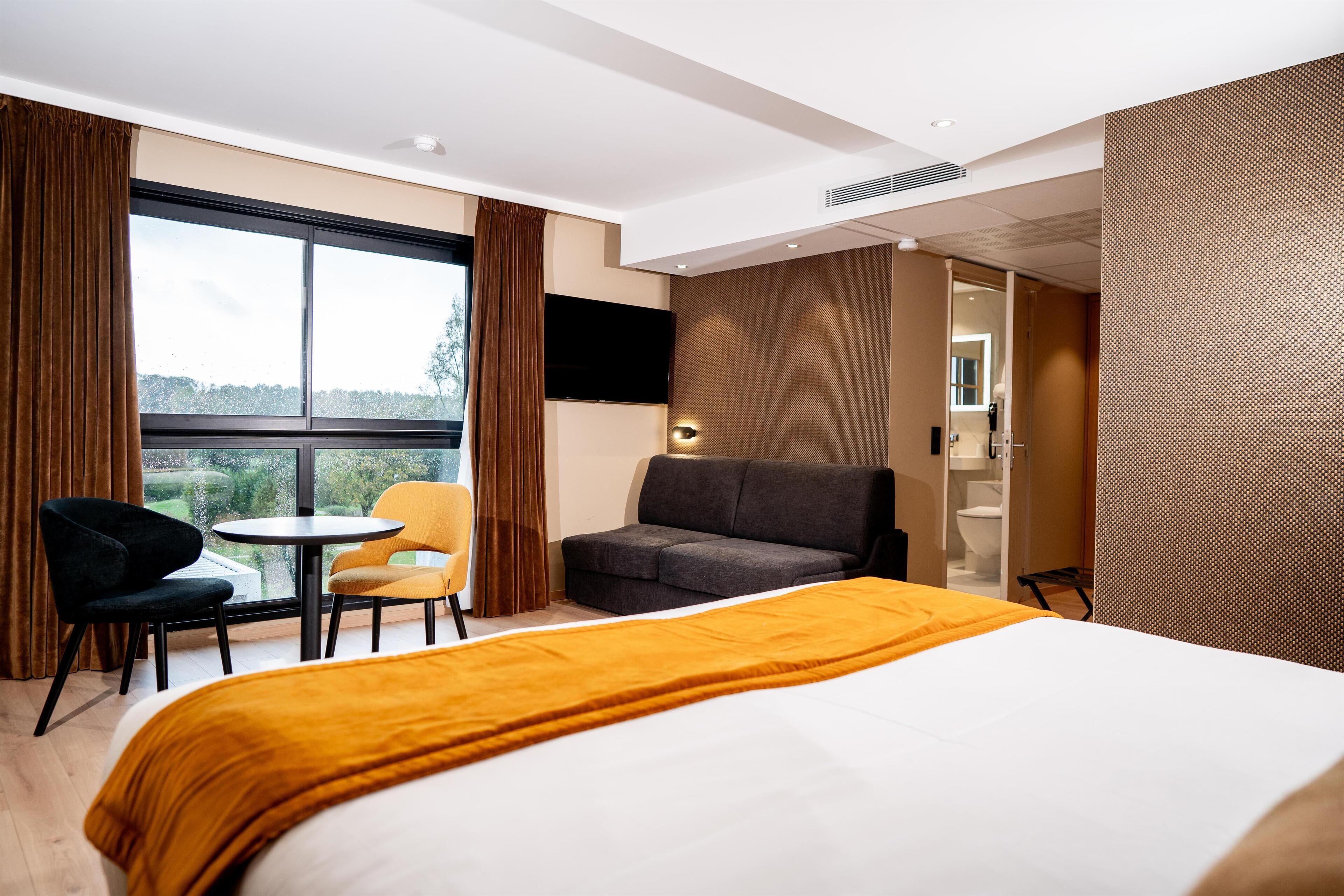 Et hotelværelse med seng, sofa, et lille bord og et fjernsyn.