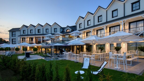 A hotel with outdoor seating, umbrellas, and a well-maintained garden.