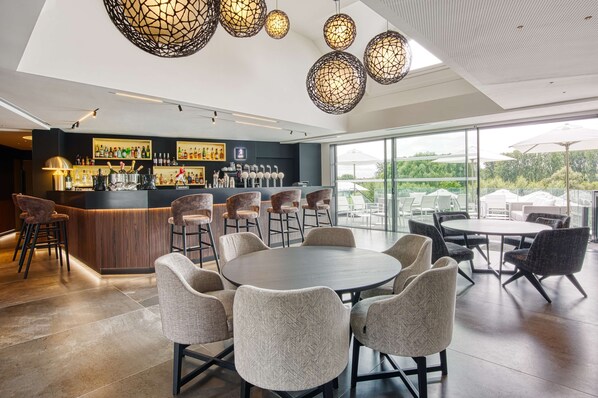 Un área de bar moderna con una barra, diversas opciones de asientos y un amplio ventanal con vistas al exterior.