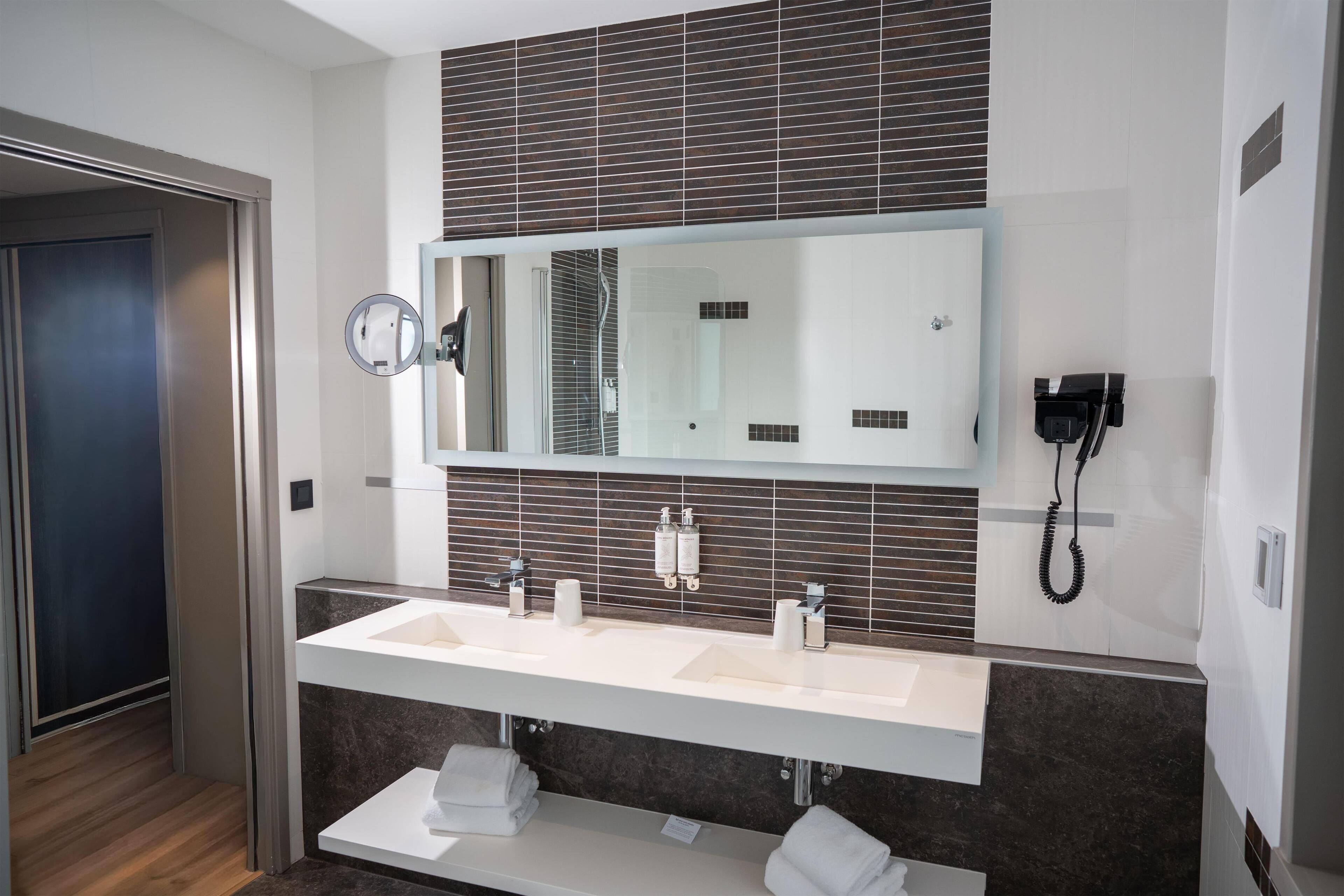 Un baño moderno con un espejo grande, dos lavamanos, un perchero para toallas y un teléfono.