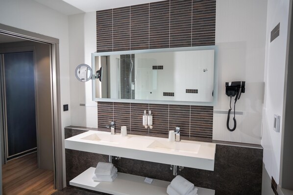 A modern bathroom with a large mirror, two sinks, a towel rack, and a telephone.