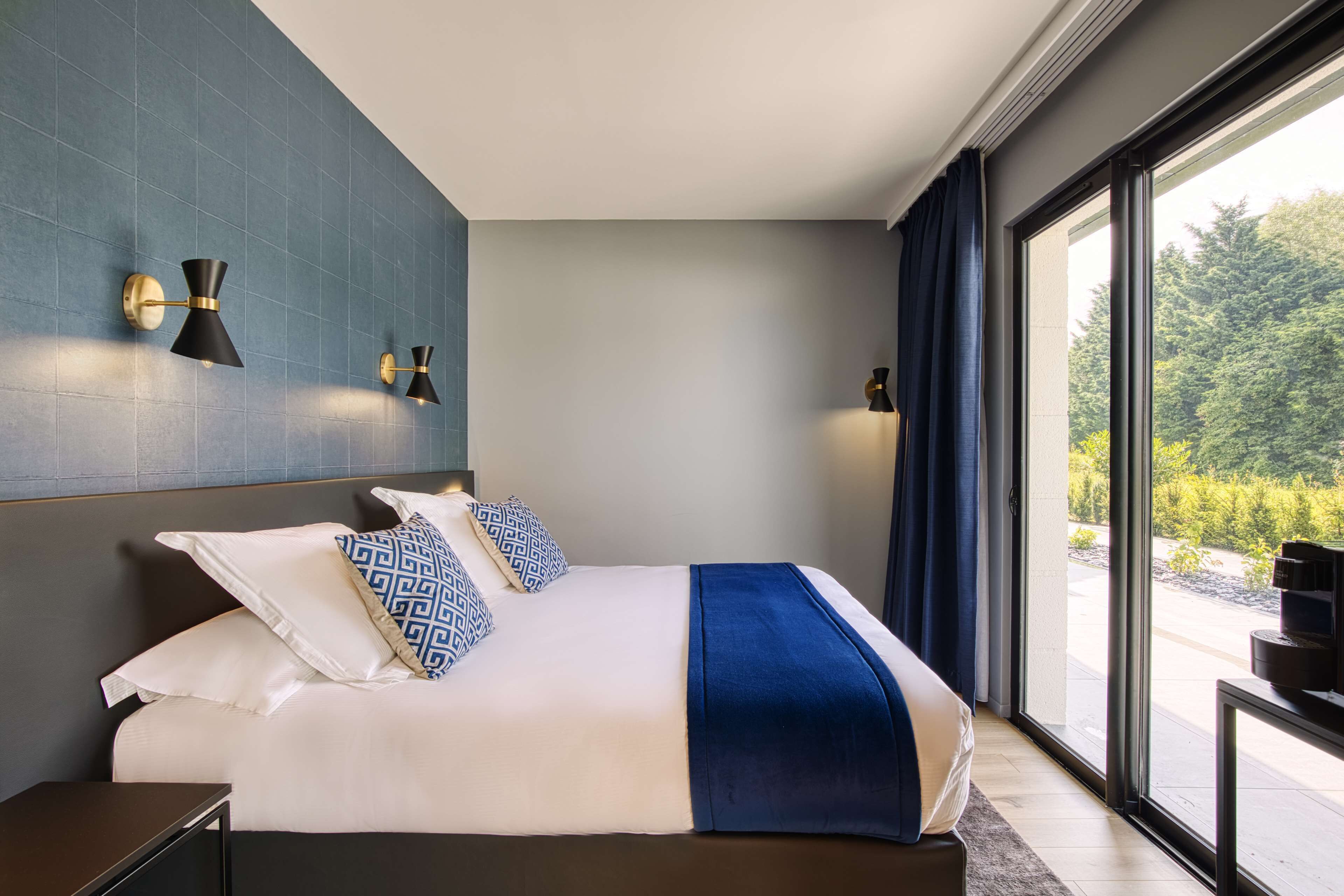 Un dormitorio moderno con una cama grande, vistas a zonas verdes y luces fijadas a la pared.