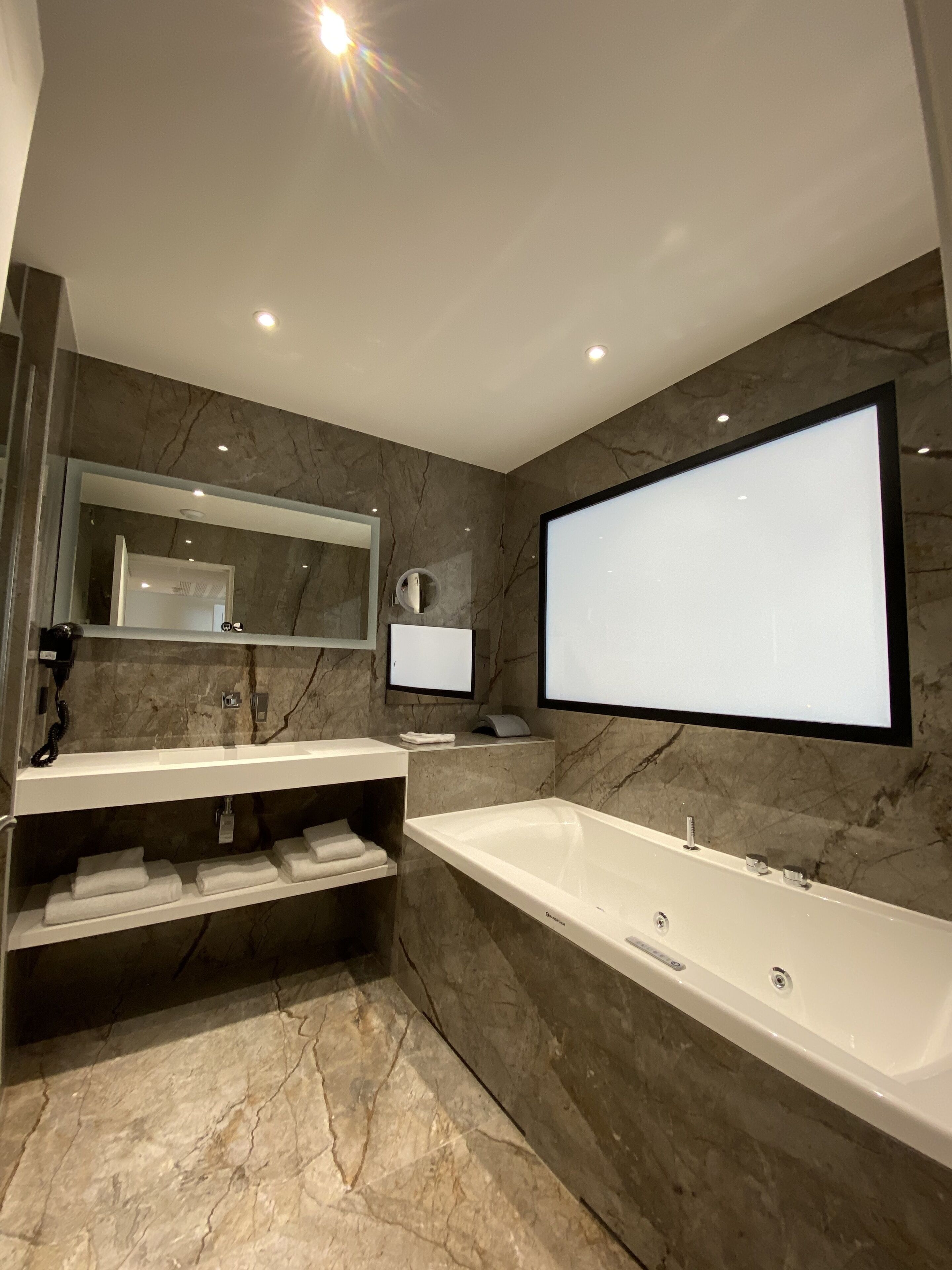 A modern bathroom with a large bathtub, a double vanity with a mirror, and marble walls.