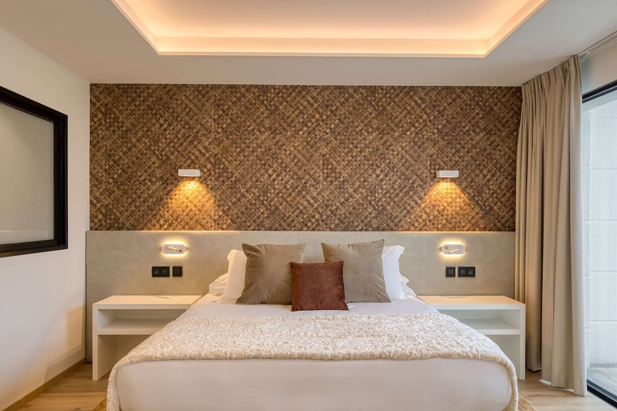 A modern bedroom with a patterned headboard, bedside lamps, and a large bed with a white cover.
