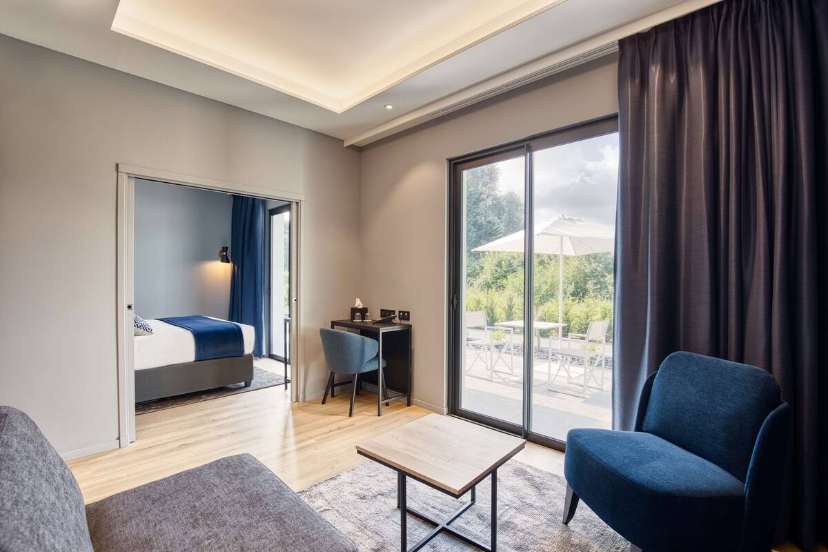 A modern hotel room with a bed, a desk, a chair, and a sofa.