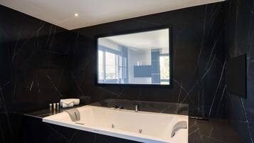 Un baño moderno con un espejo grande, una bañera y paredes de mármol negro.