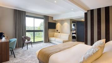 Habitación de hotel con una cama grande, un escritorio, una silla, un sofá y un televisor.