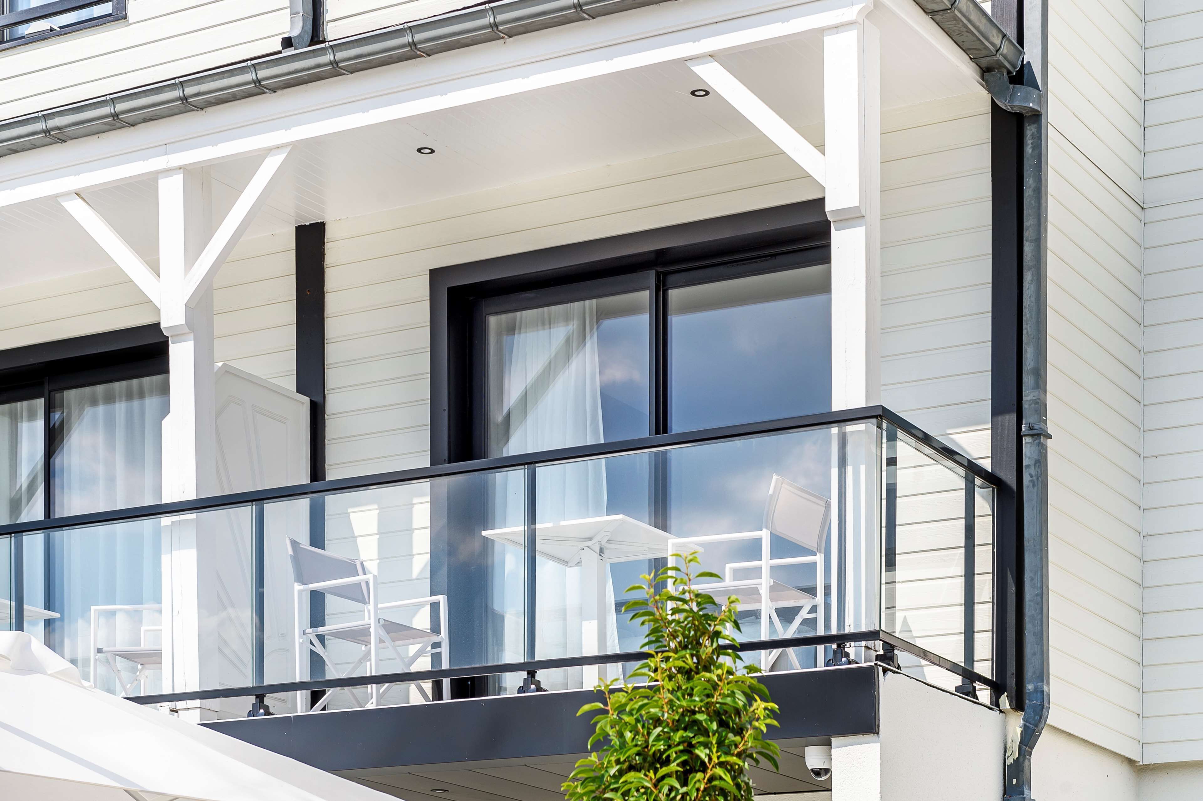 Un bâtiment moderne doté d’un balcon agrémenté de chaises blanches et d’une petite plante en pot.