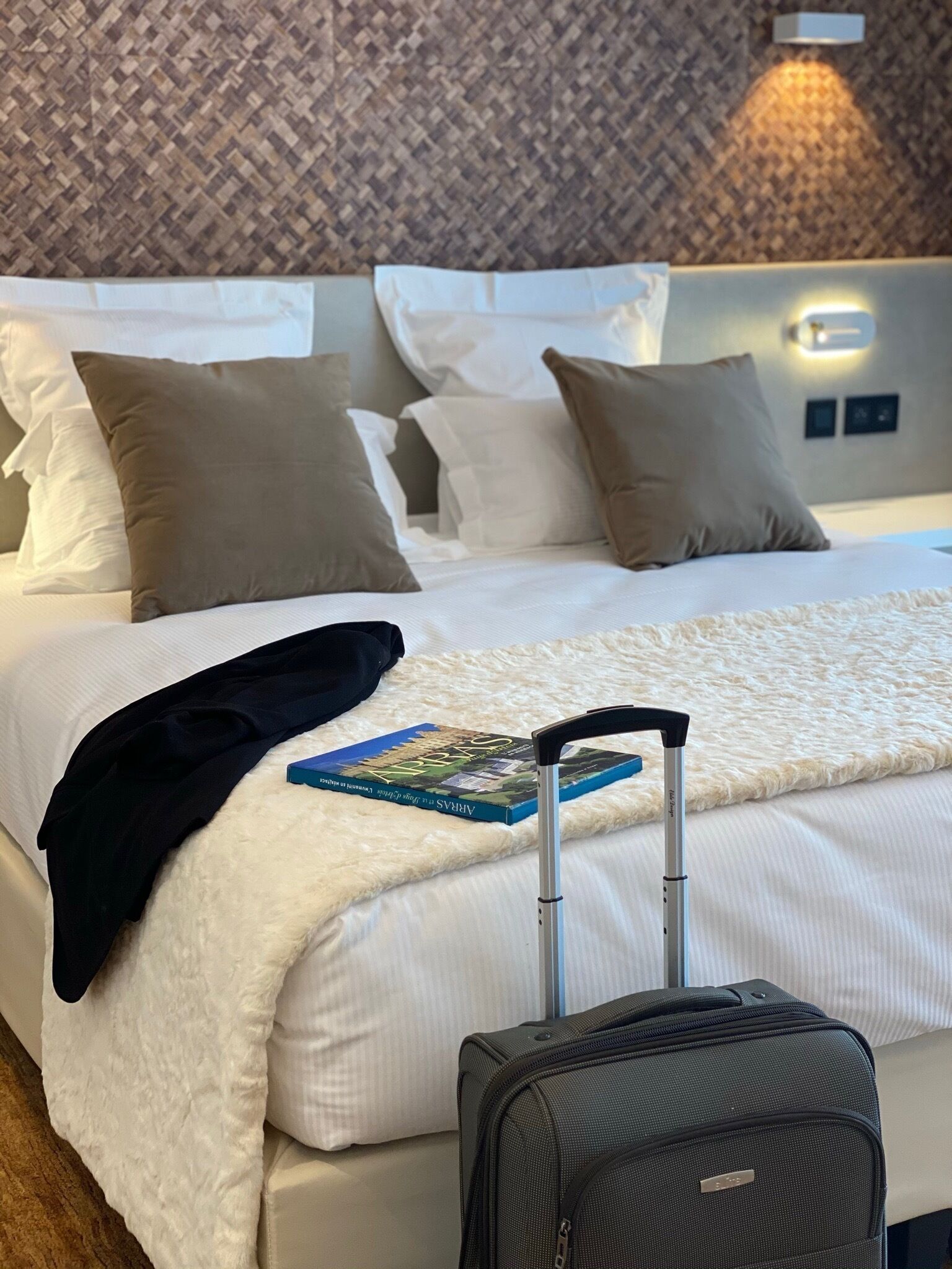 A hotel room with a neatly made bed, a book, and a suitcase.