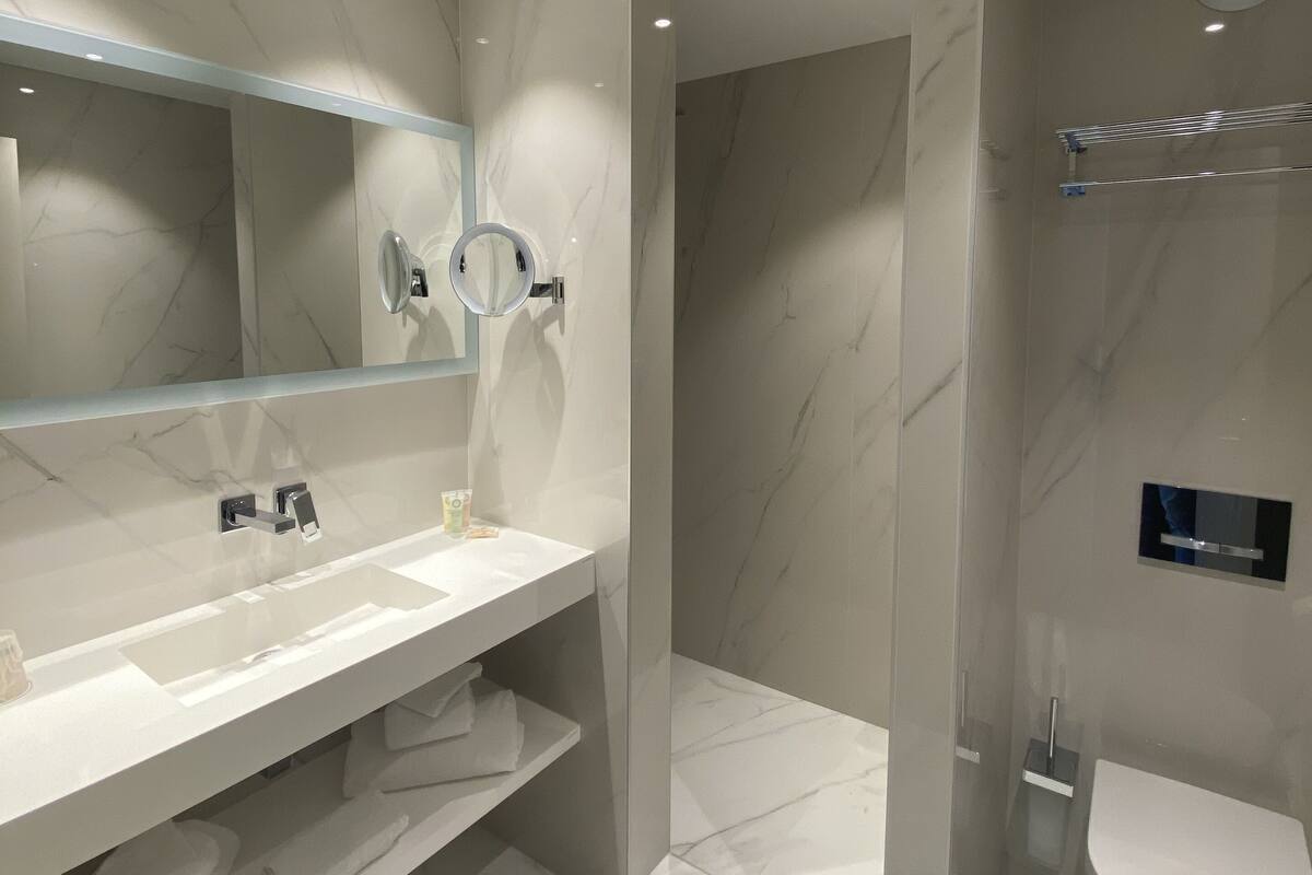 A modern bathroom with a large mirror, white marble walls, a white sink, and a toilet.
