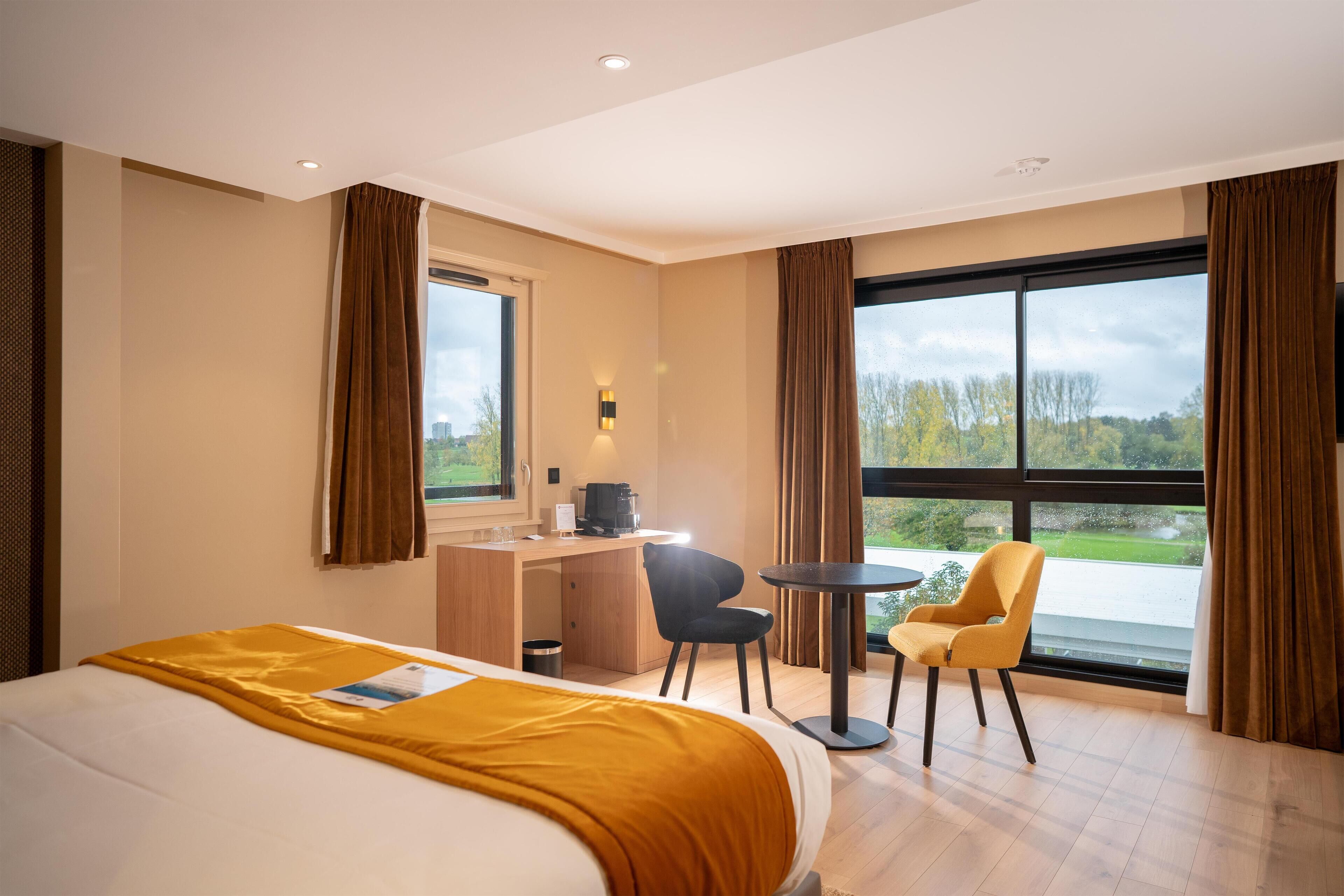 A hotel room with a large bed, a desk, a chair, and a view of the outdoors.