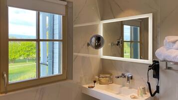 A bathroom with a large mirror, a vanity with a sink, and a window offering a view of greenery.
