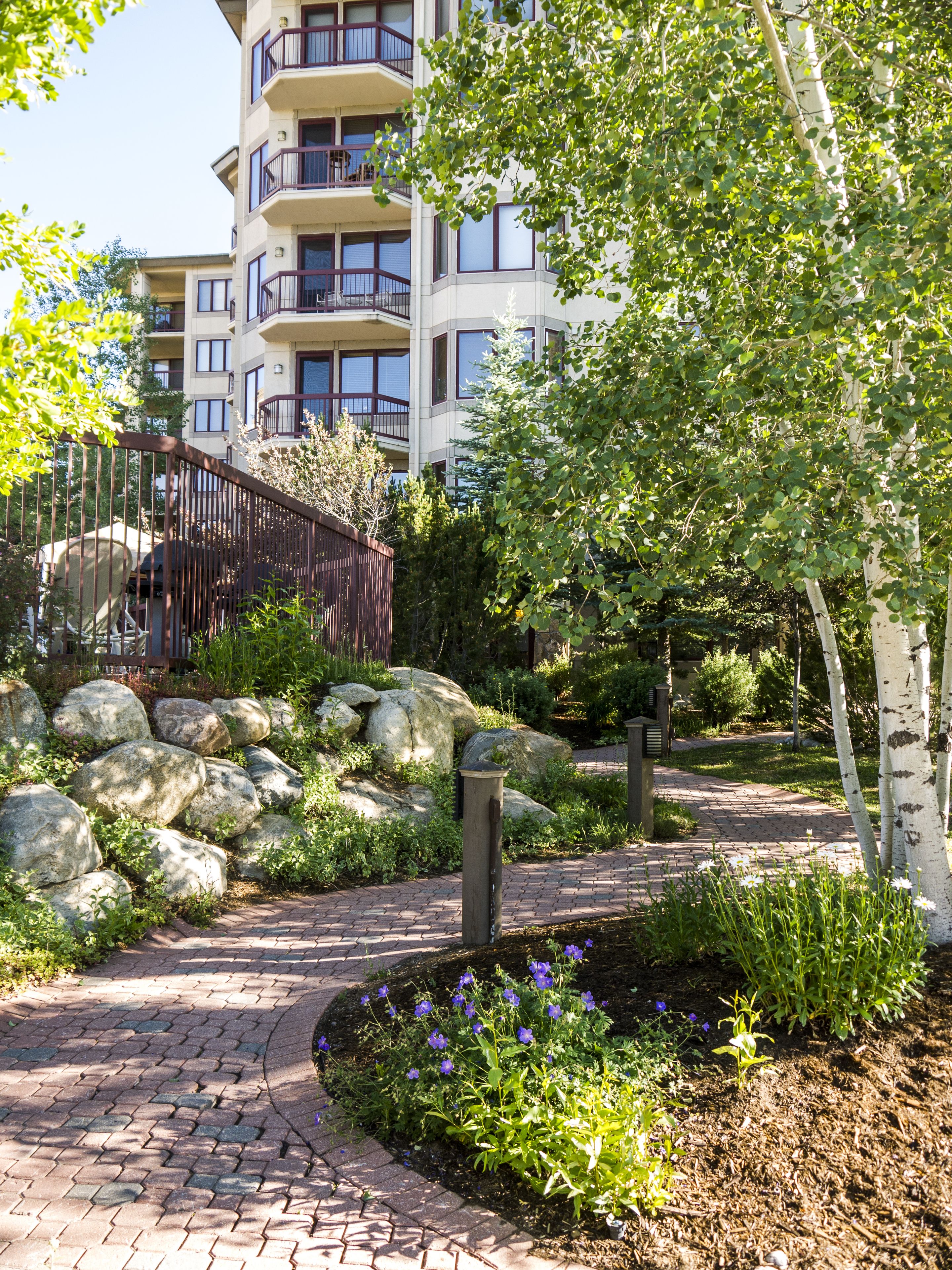 A landscaped pathway with large rocks, a wooden fence, and a variety of plants.