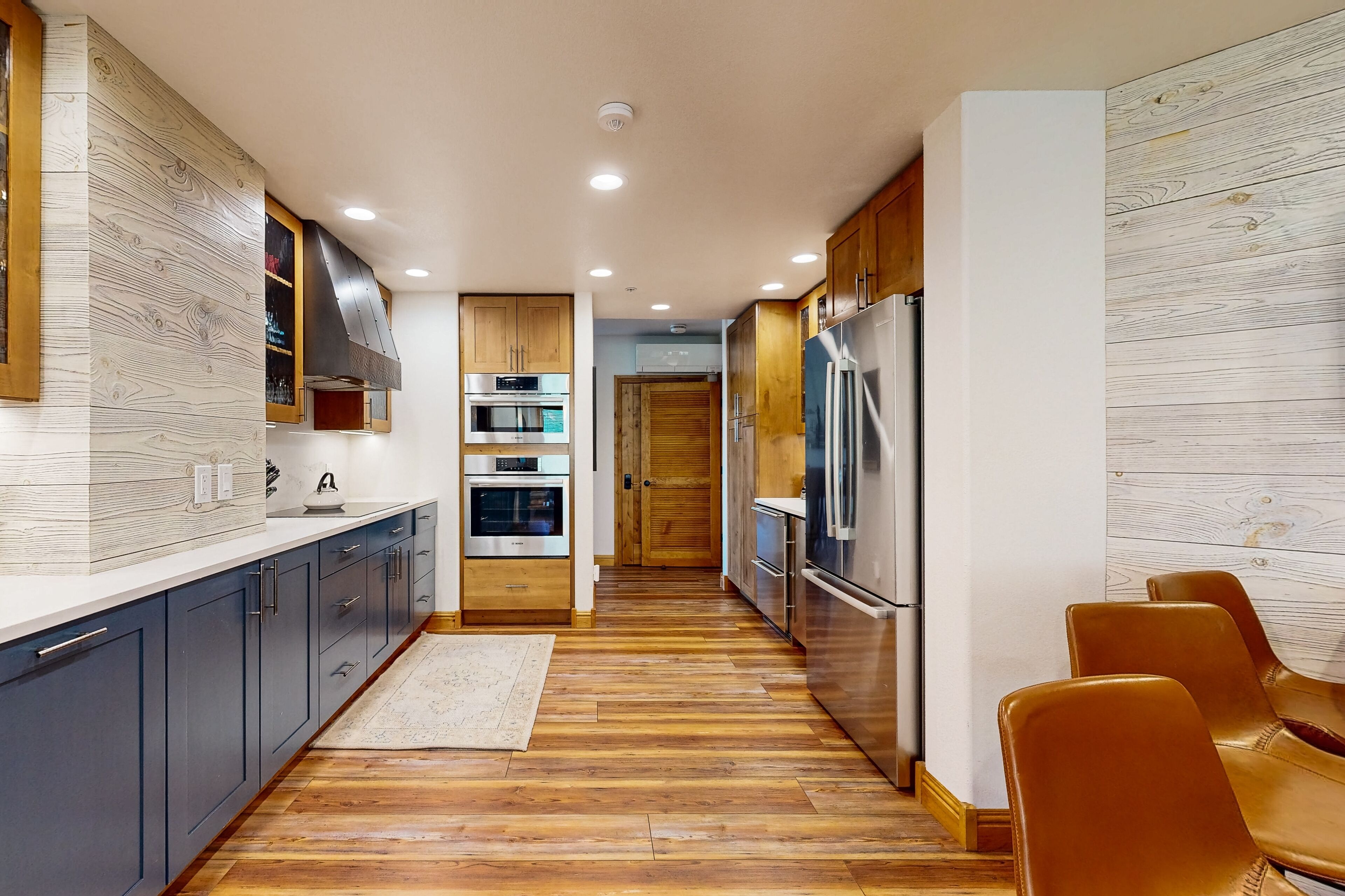 A modern kitchen with wooden flooring, stainless steel appliances, and dark blue cabinets.
