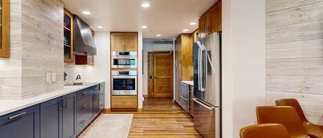 A modern kitchen with wooden flooring, stainless steel appliances, and dark blue cabinets.