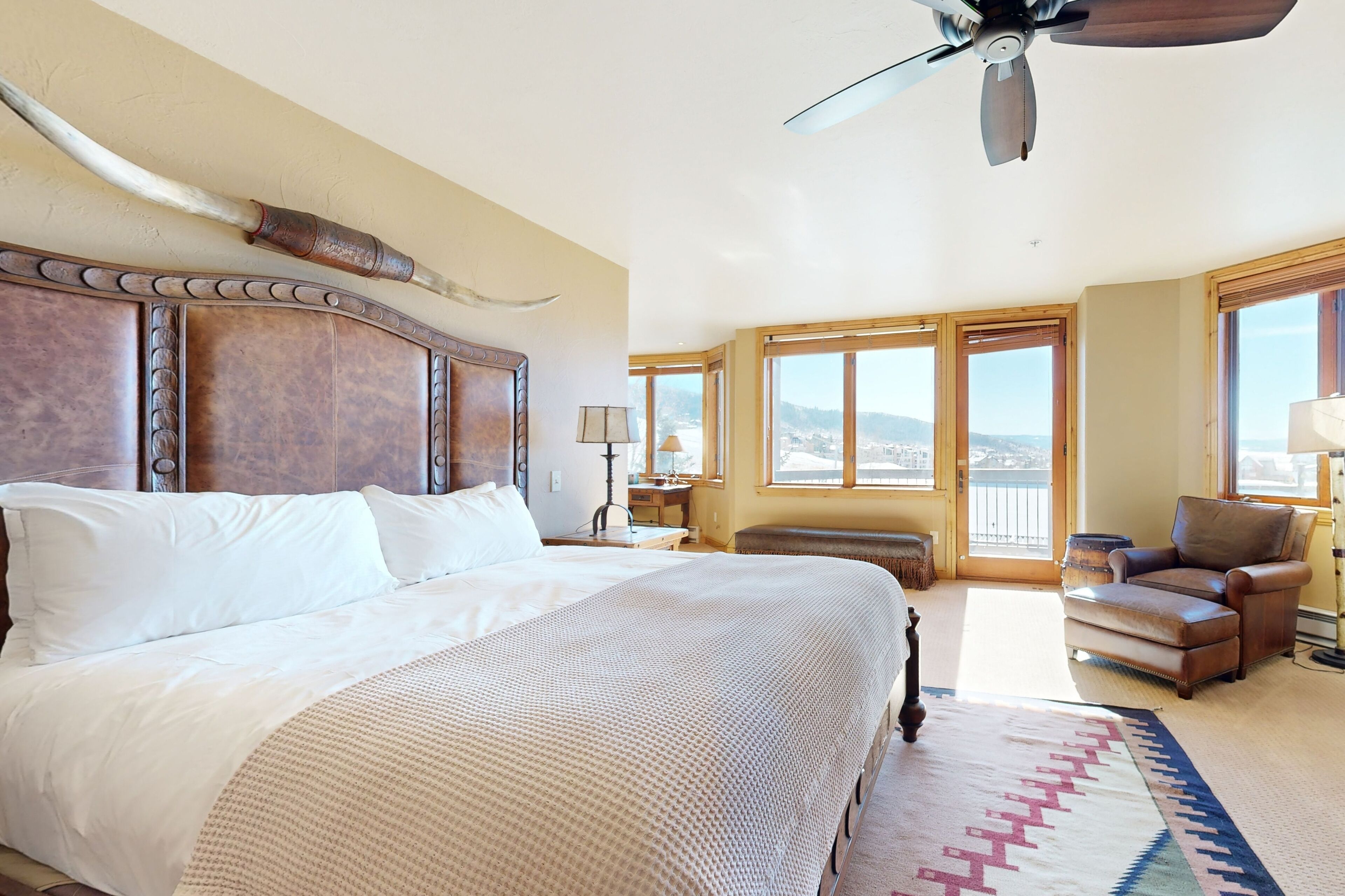A spacious bedroom with a large bed, a ceiling fan, and a view of the outdoors through large windows.