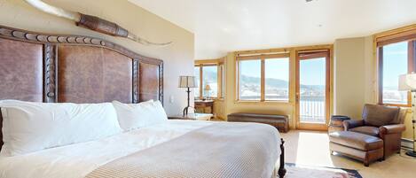 A spacious bedroom with a large bed, a ceiling fan, and a view of the outdoors through large windows.