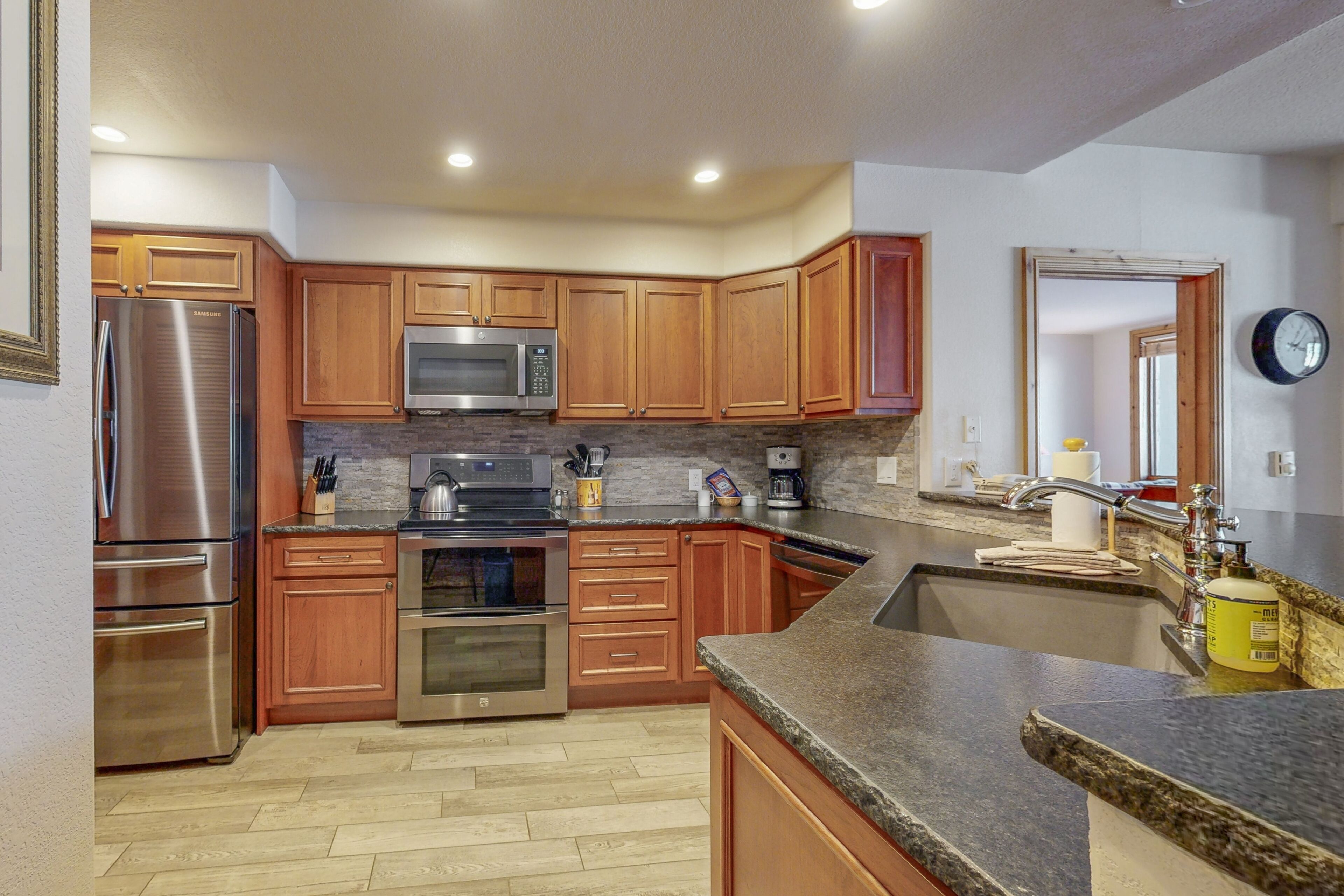 A modern kitchen with wooden cabinets, stainless steel appliances, granite countertops, and a built-in oven.