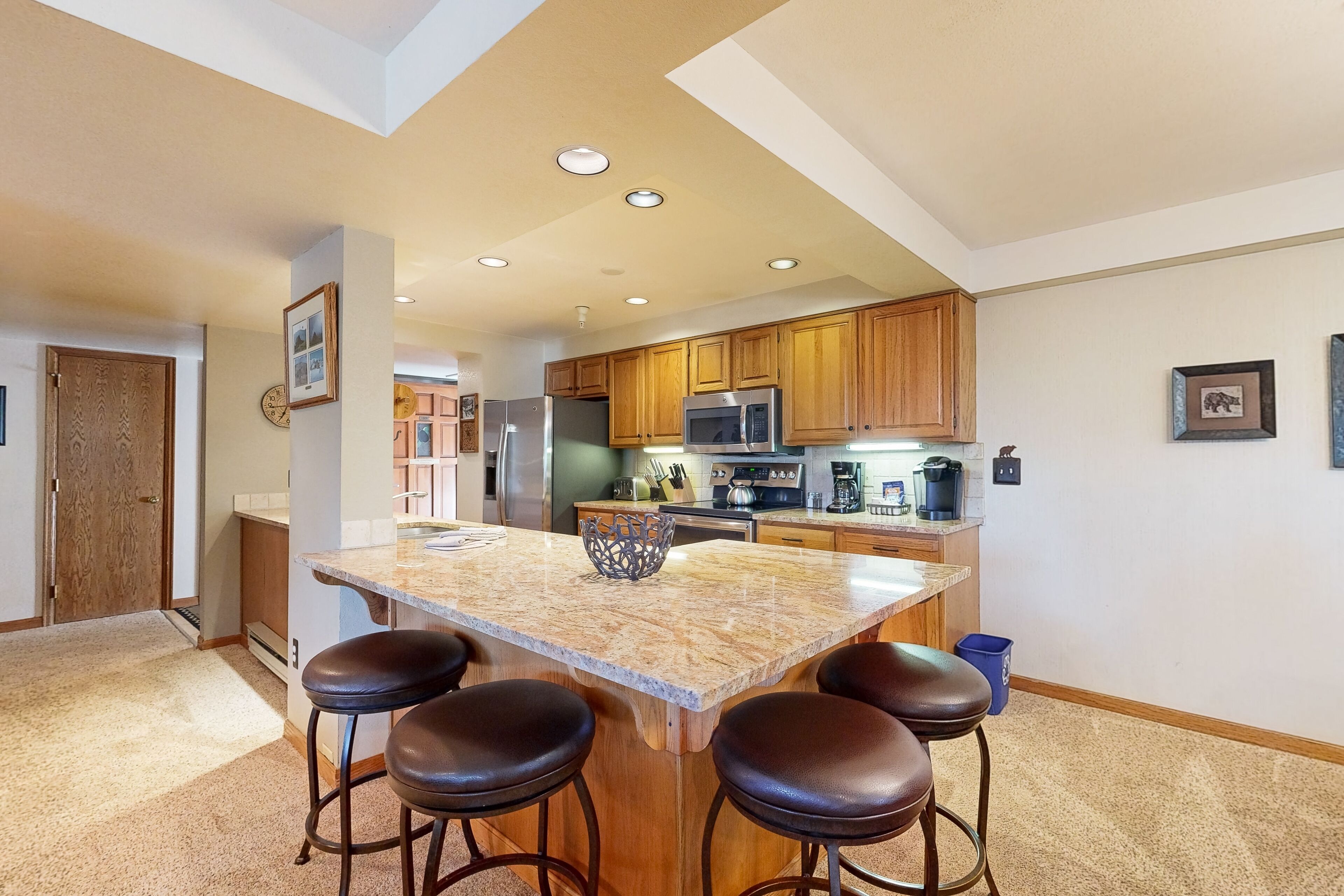 A modern kitchen with wooden cabinets, a central island with stools, and built-in appliances.