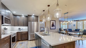 A modern kitchen with stainless steel appliances, a large island, and pendant lighting. - Torian Plum Condominiums (Steamboat Springs)