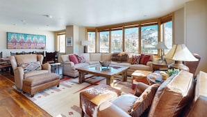 A spacious living room with a large window, a sofa set, a coffee table, and a painting on the wall. - Torian Plum Condominiums (Steamboat Springs)