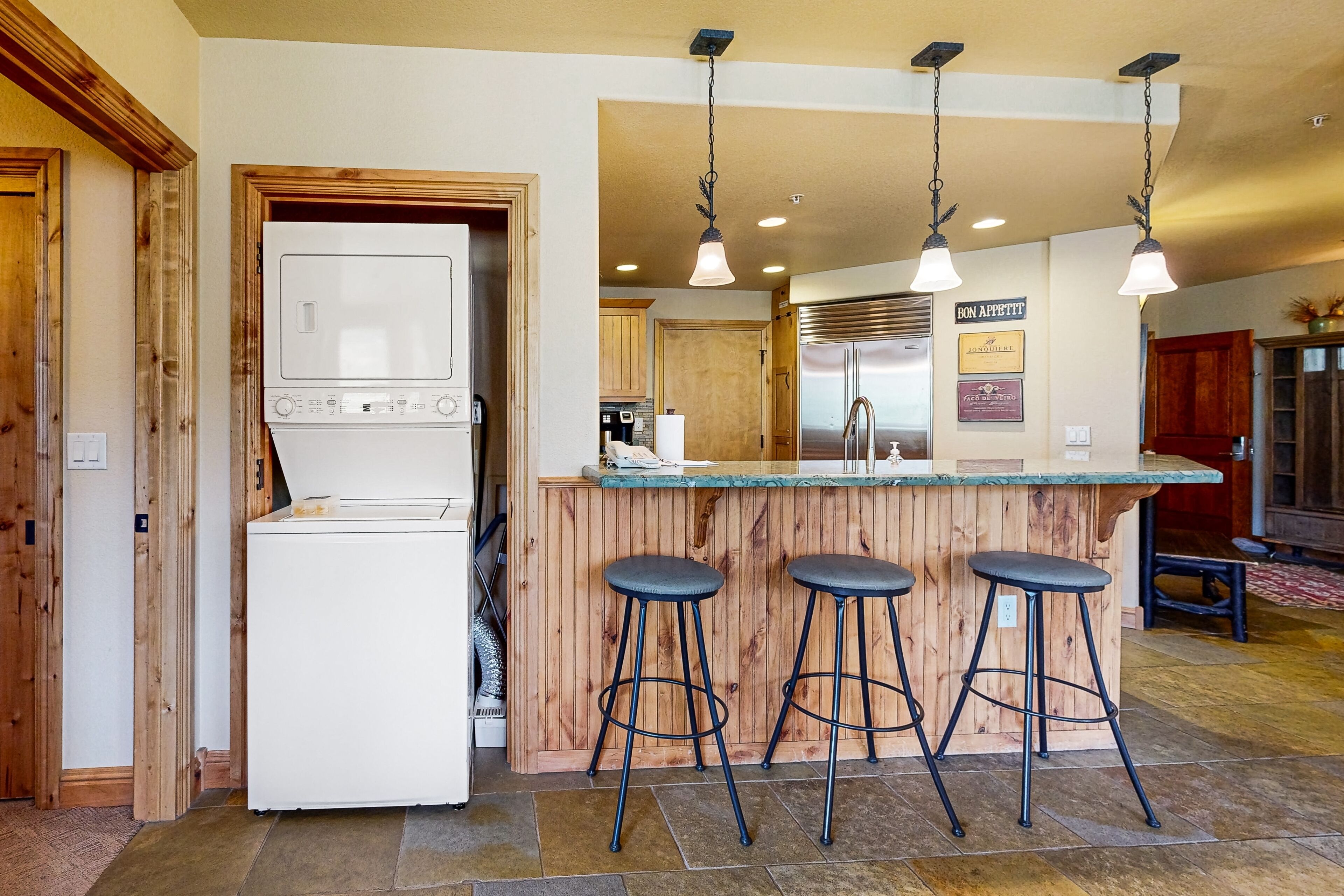 A kitchen with a white refrigerator, wooden cabinets, a bar area with stools, and pendant lighting.
