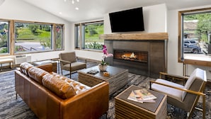 A modern living room with a fireplace, leather sofa, and large windows offering a view of the outdoors. - Torian Plum Condominiums (Steamboat Springs)