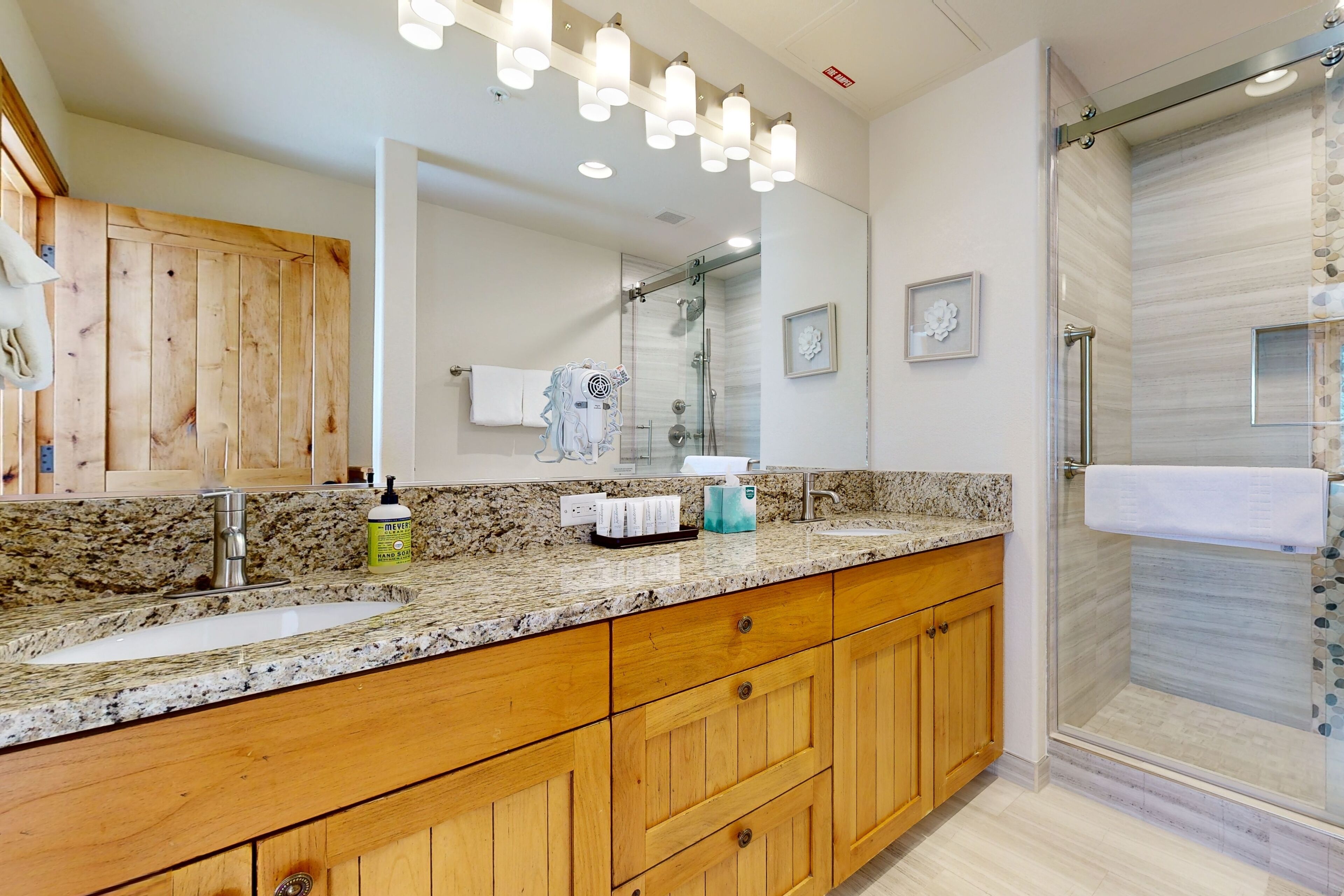 Une salle de bain moderne avec un comptoir en granit, des meubles en bois, un grand miroir et une cabine de douche en verre.