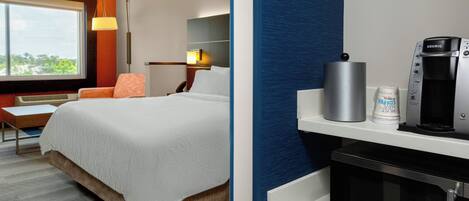 A hotel room with a bed, a desk, a chair, a lamp, a coffee maker, a microwave, and a window with a view.