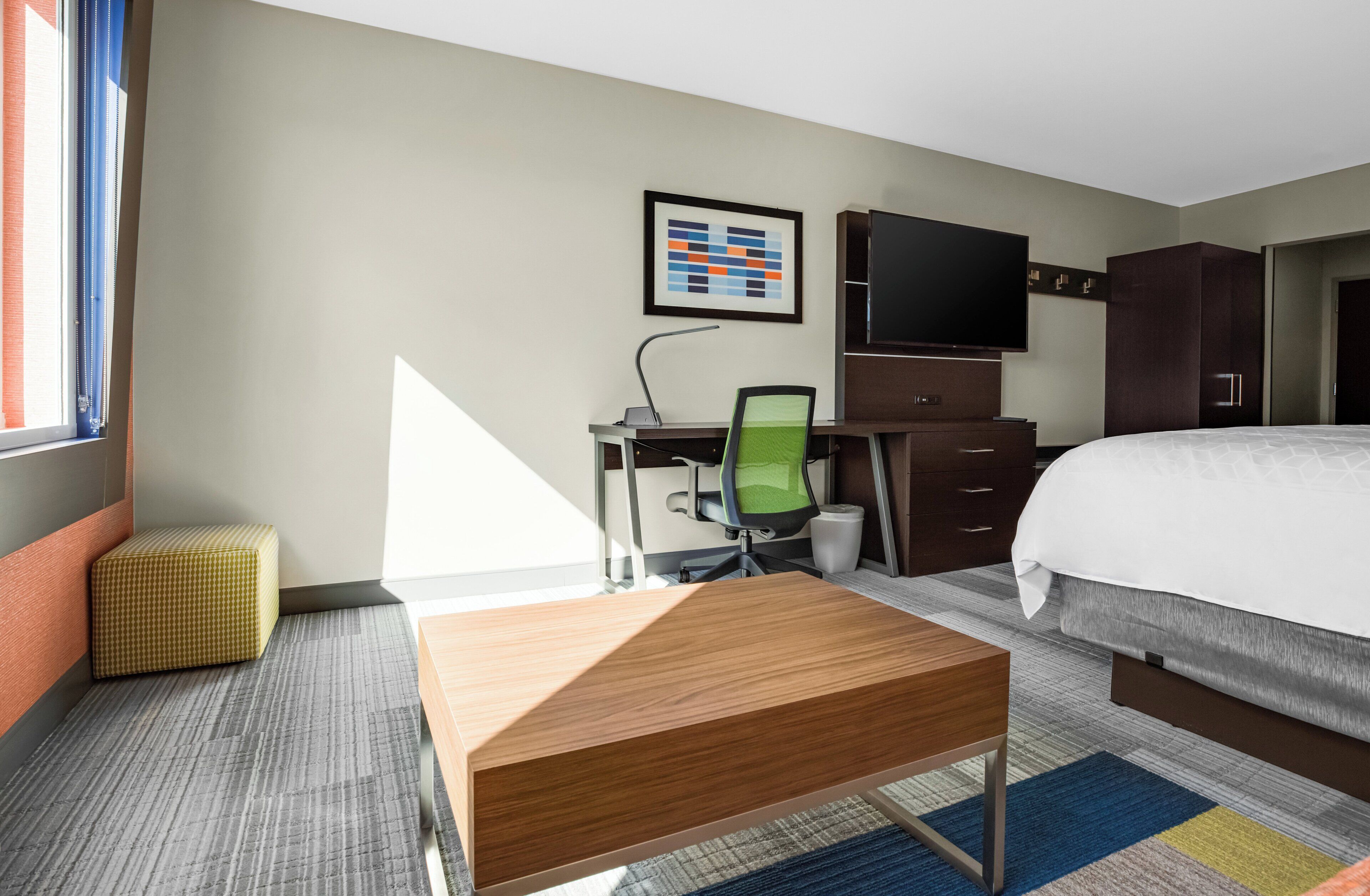 Ein Hotelzimmer mit Bett, Schreibtisch, Stuhl, Fernseher, Kleiderschrank und Fenster.