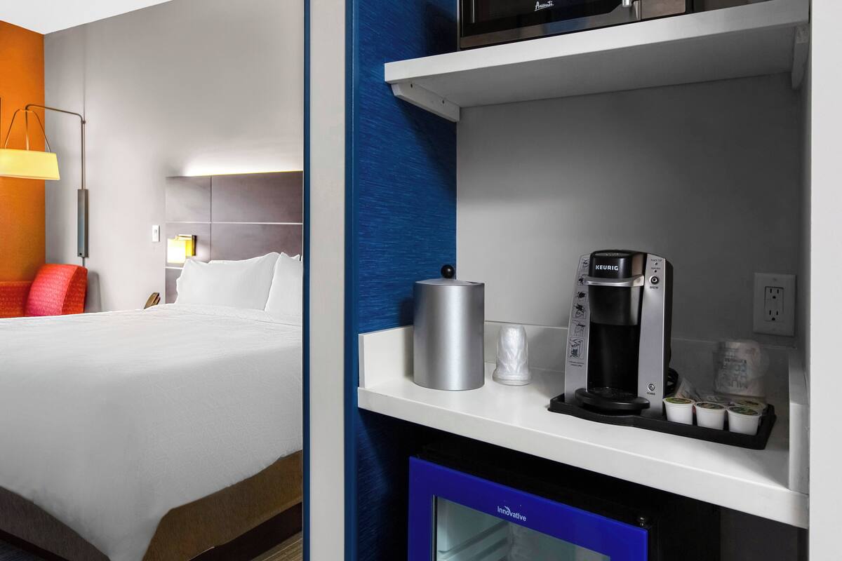A hotel room with a bed, a coffee machine, and a small refrigerator.