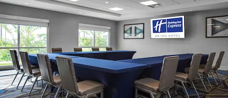 Un salón de conferencias con una larga mesa y sillas, ventanas grandes y un cartel de Holiday Inn Express en la pared.