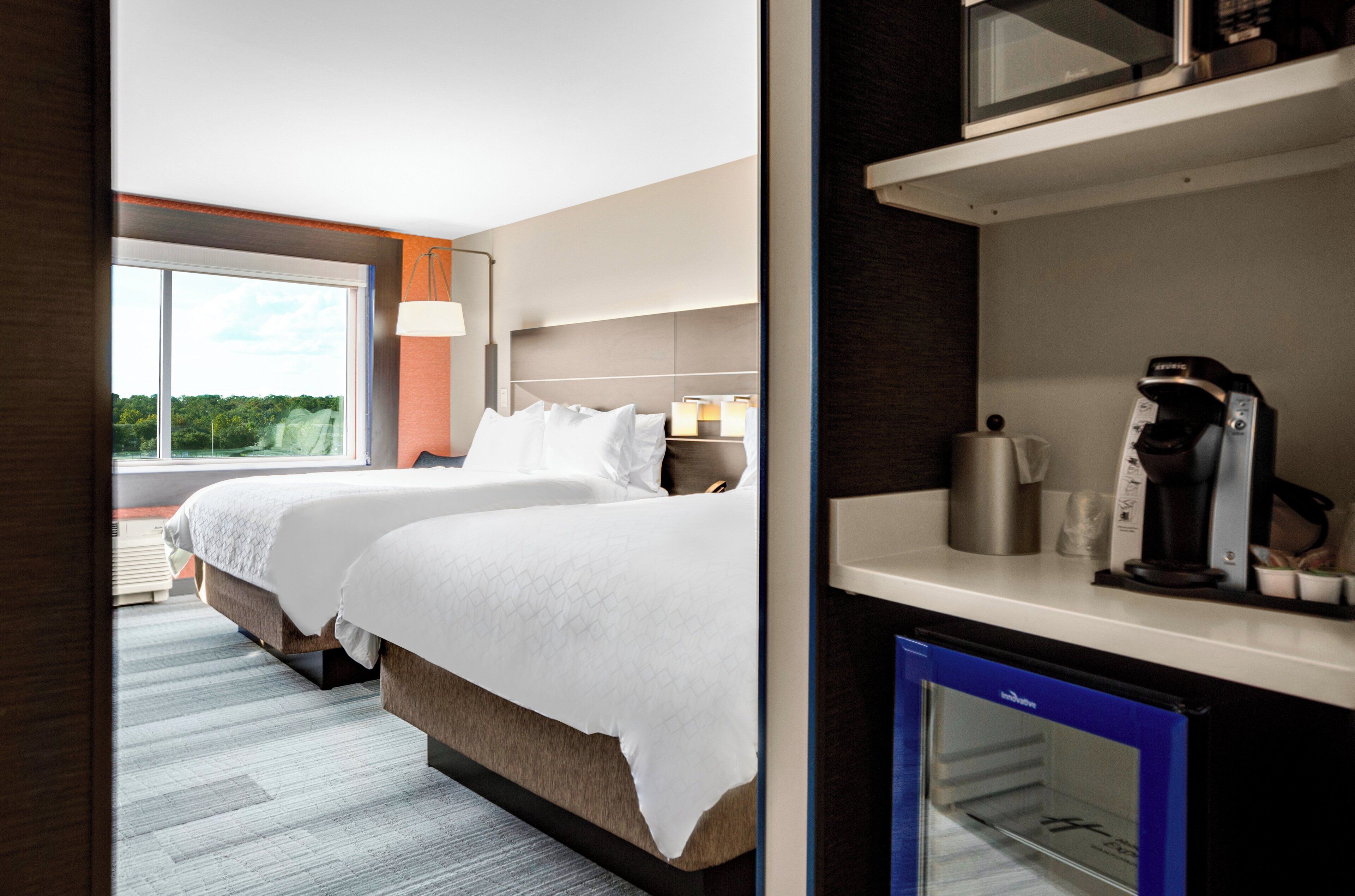 A hotel room with a large bed, bedside tables, a coffee machine, and a view of greenery outside.