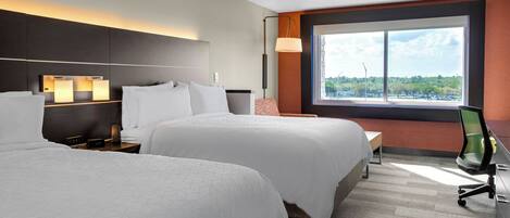 A hotel room with two beds, a desk, a chair, and a large window with a view.