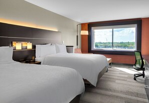 Habitación de hotel con dos camas, un escritorio, una silla y un amplio ventanal con vistas.