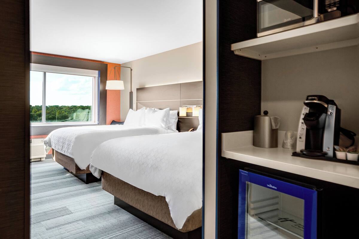 A hotel room with a large bed, bedside tables, a coffee machine, and a view of greenery outside.