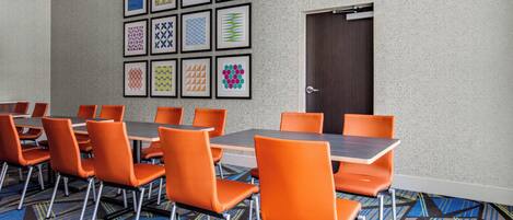 A conference room with orange chairs and tables, a patterned carpet, and a wall with framed geometric designs.