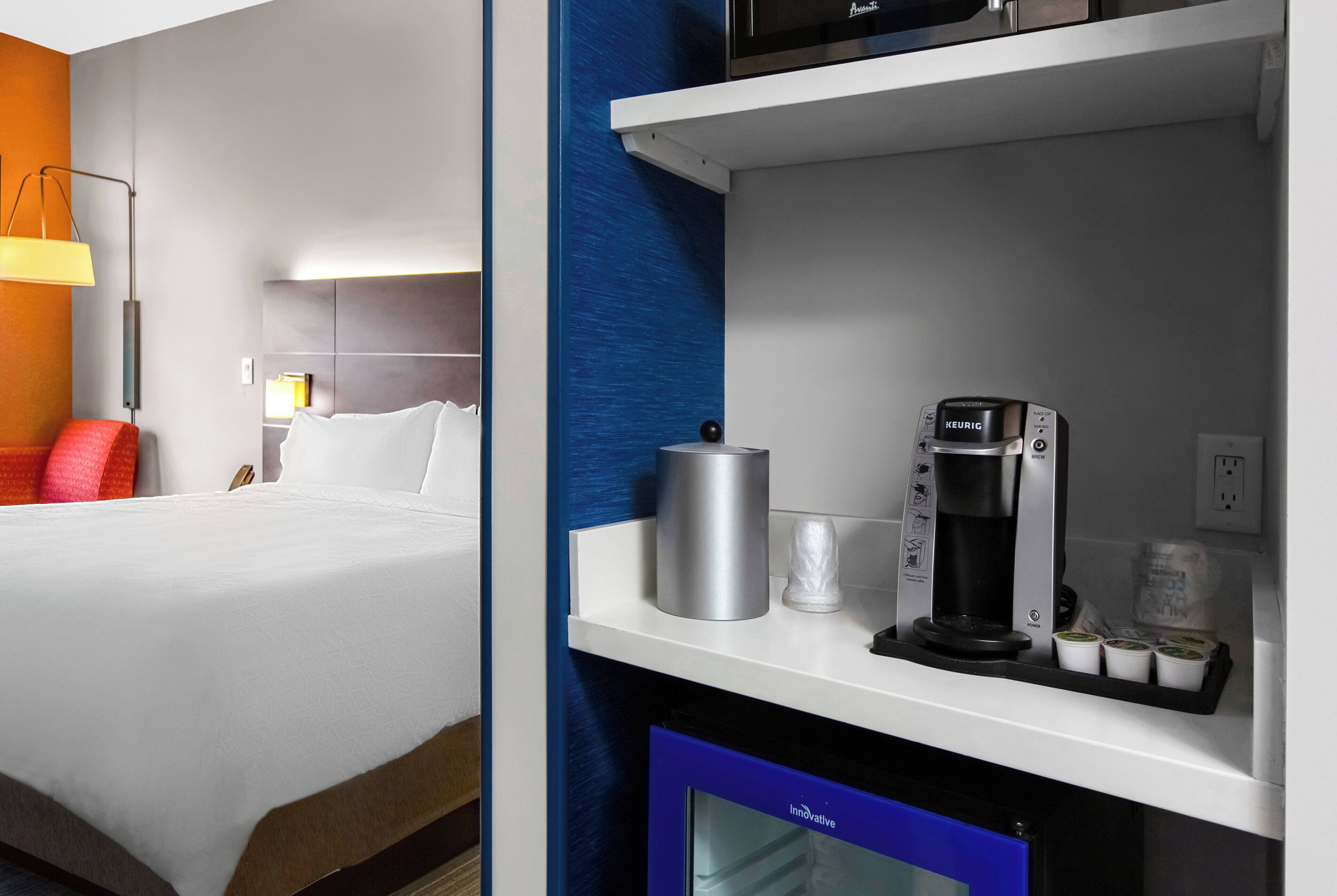 A hotel room with a bed, a coffee machine, and a small refrigerator.