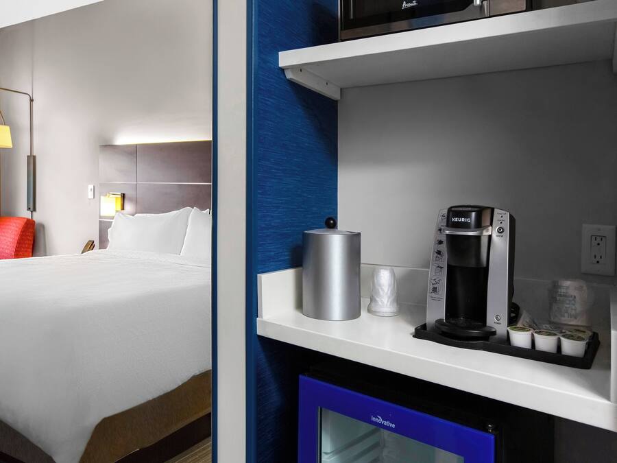 A hotel room with a bed, a coffee machine, and a small refrigerator.