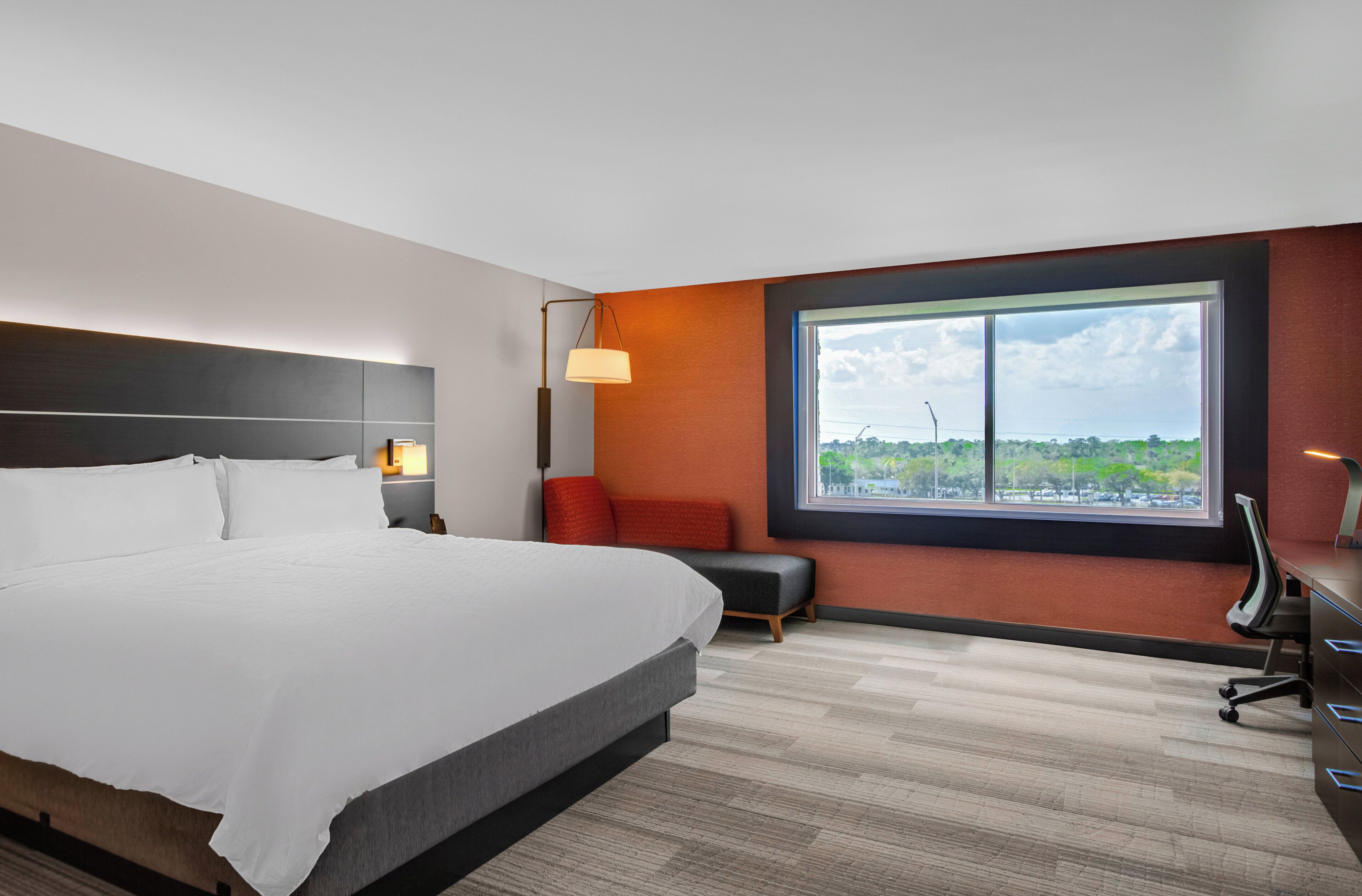 Une chambre d’hôtel avec un grand lit, un bureau, une chaise, une lampe et une fenêtre donnant sur un beau paysage.