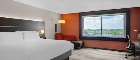 A hotel room with a large bed, a desk, a chair, a lamp, and a window with a view.